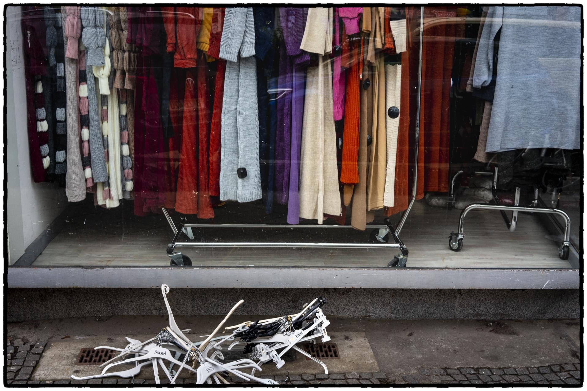Färgglada kläder i skyltfönster med galgar utslängda på trottoaren