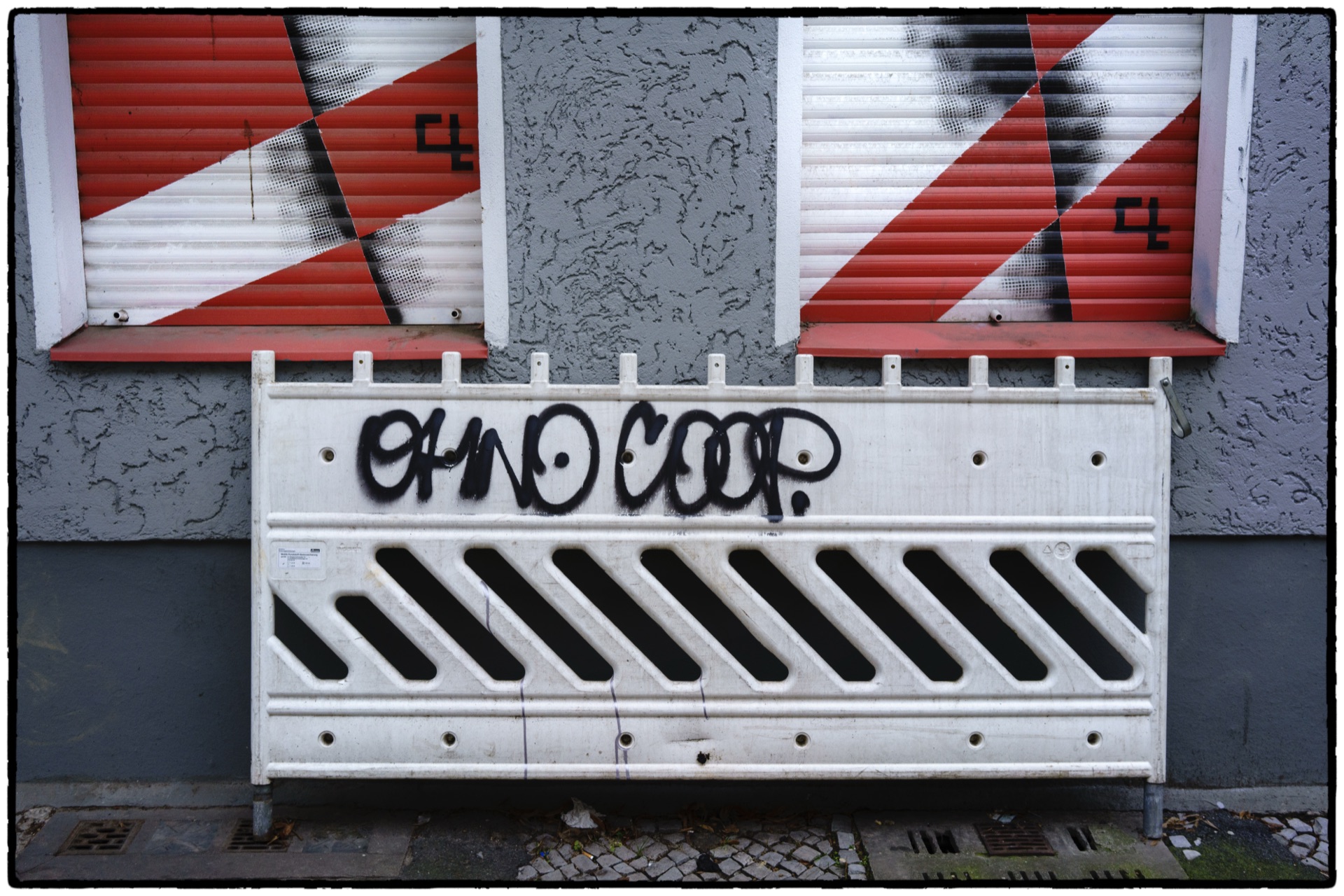 Vägbarriär med graffiti framför rödvita randiga fönsterluckor