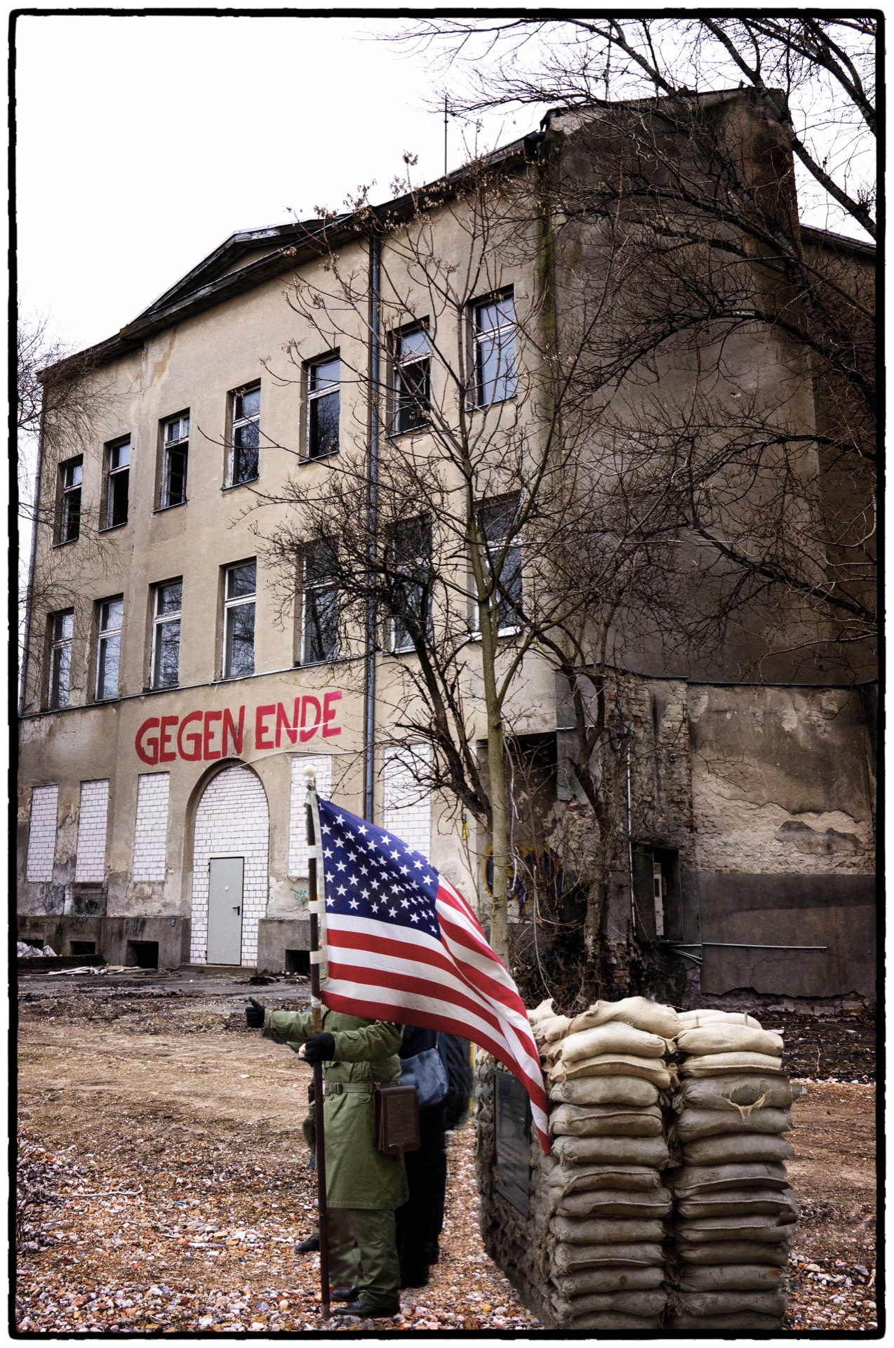 Amerikansk flagga och sandsäckar vid övergiven byggnad, texten Gegen Ende