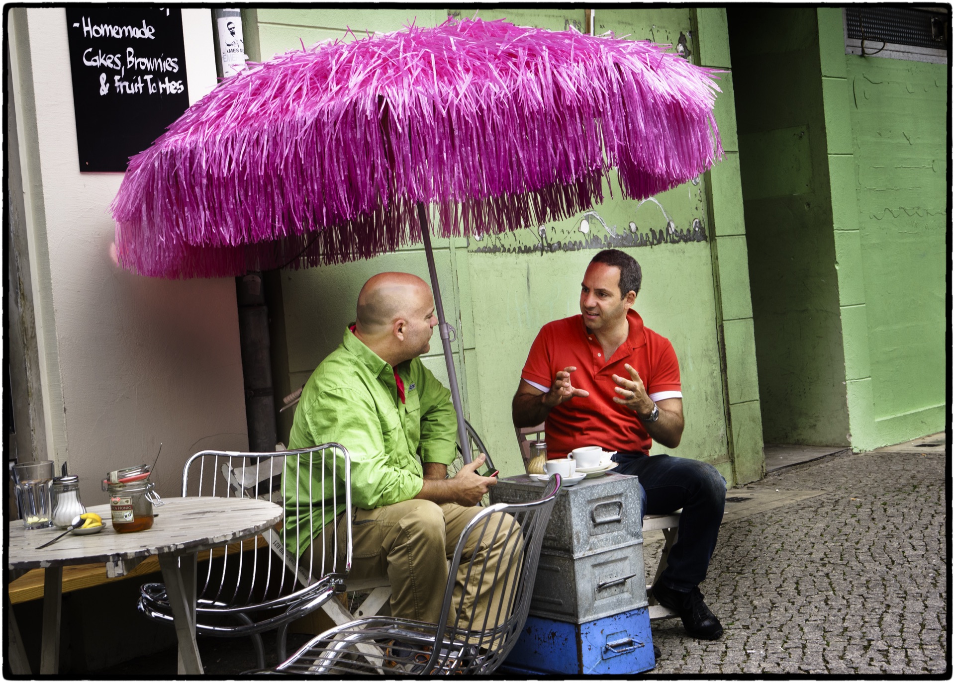 Två män samtalar under rosa parasoll vid gatukafé