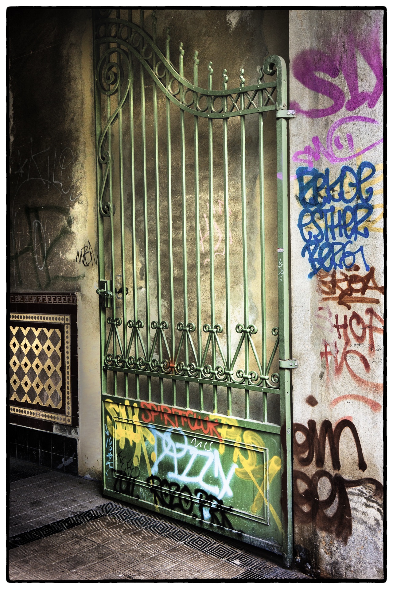Grön smidesgrind med graffiti bredvid kakeldetaljer i port