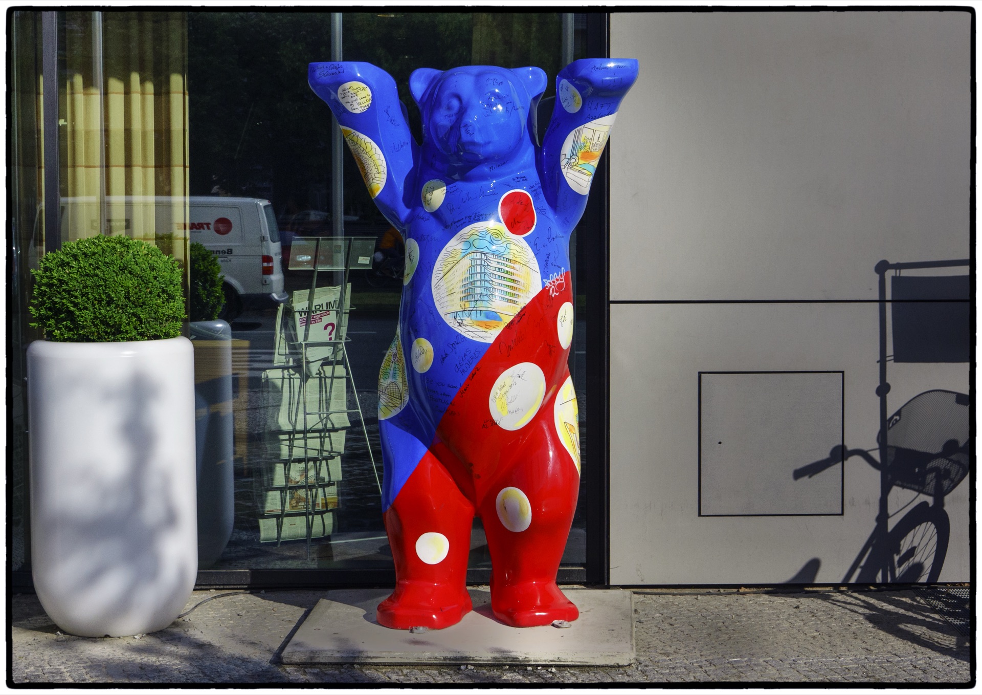 Blåröd Buddy Bear-skulptur framför glasfasad