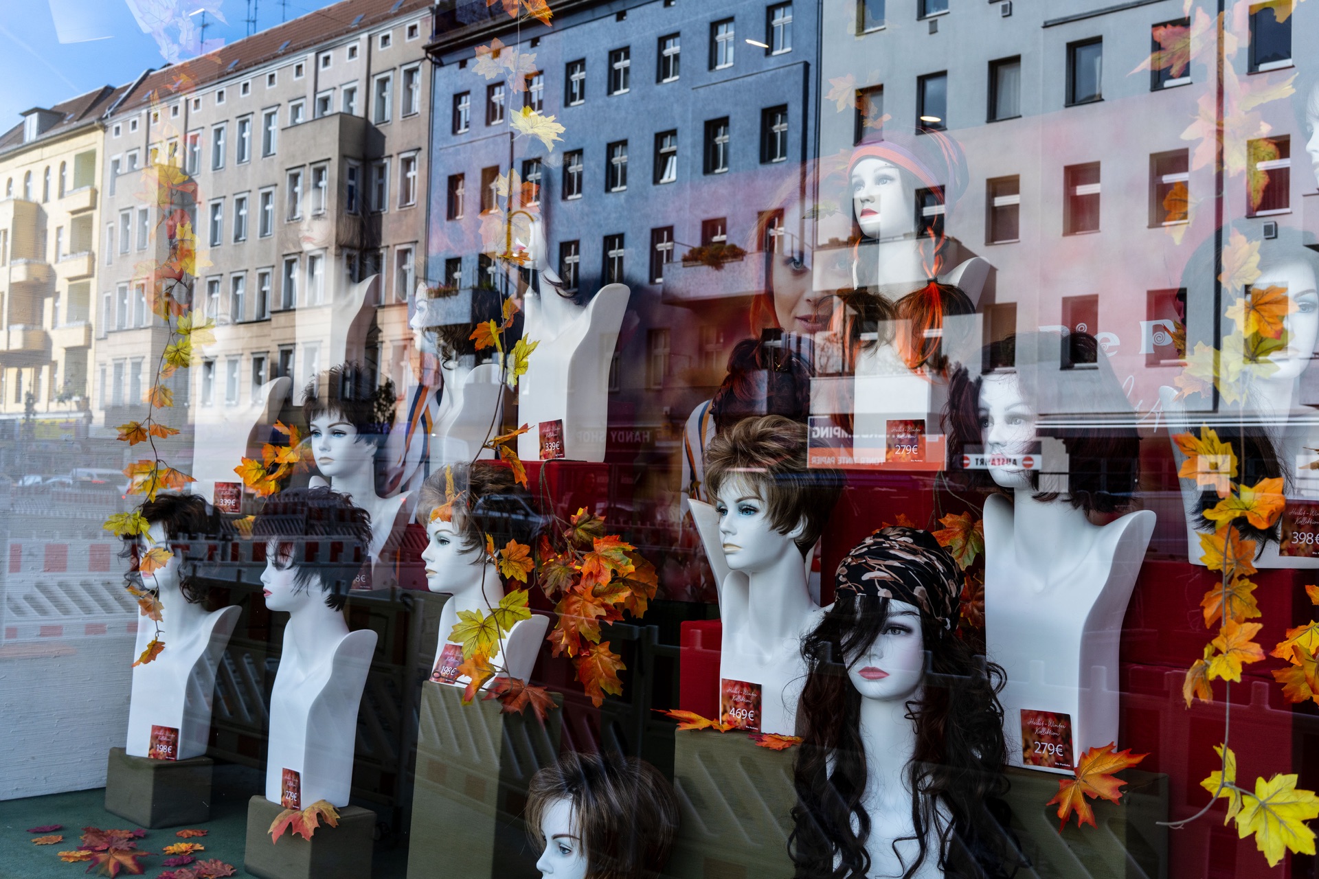 Perukdockor i skyltfönster med höstlöv och fasadreflektioner