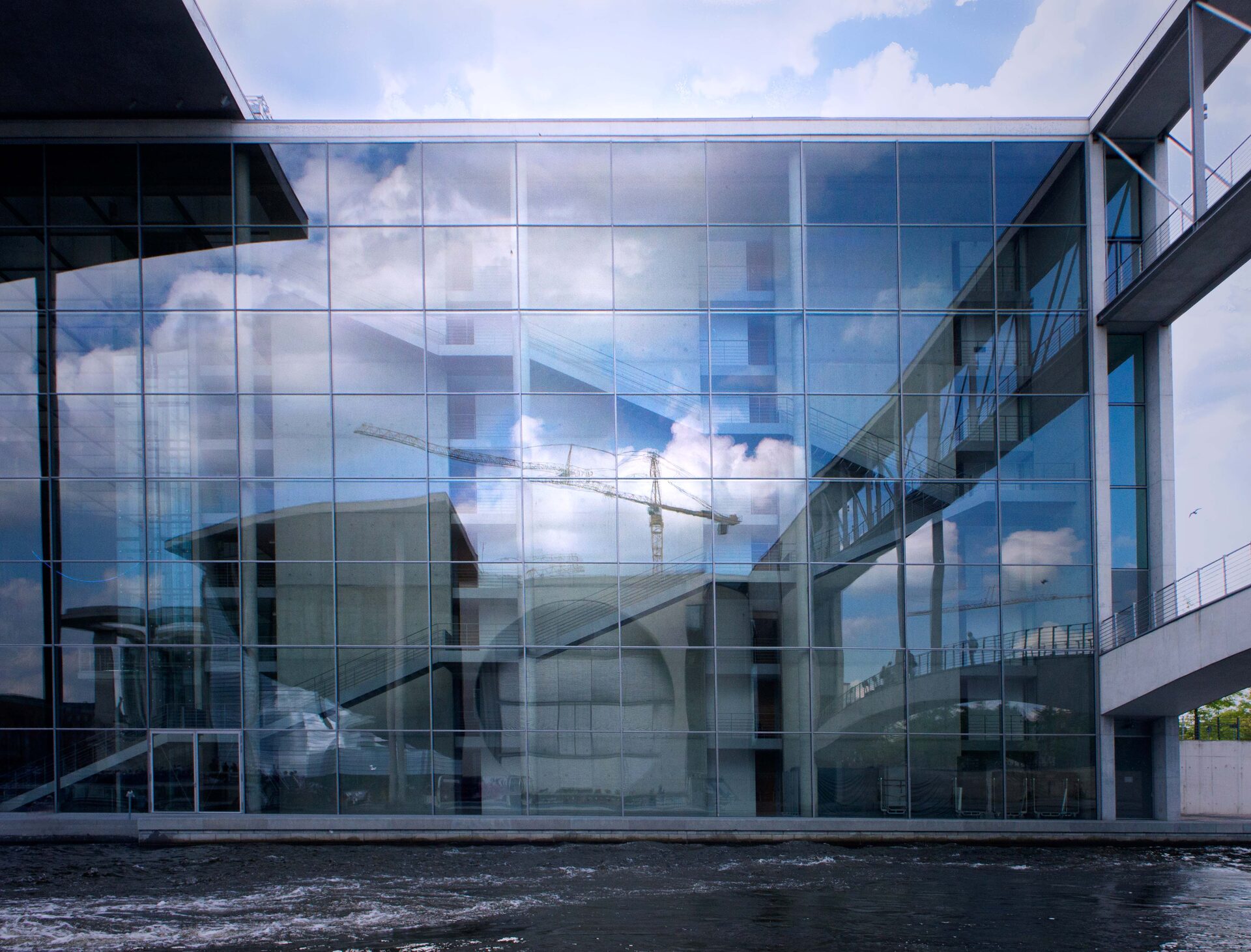 Modern glasfasad speglar moln och byggnader vid Spree