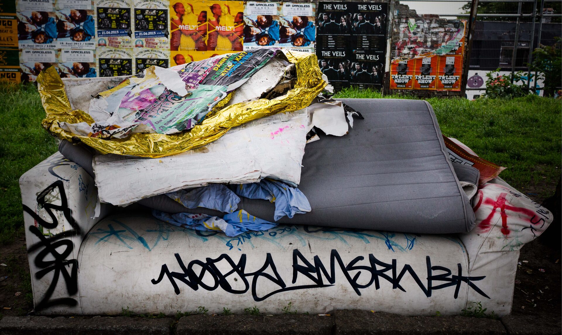 Övergiven soffa med graffiti och affischer på gräsmatta