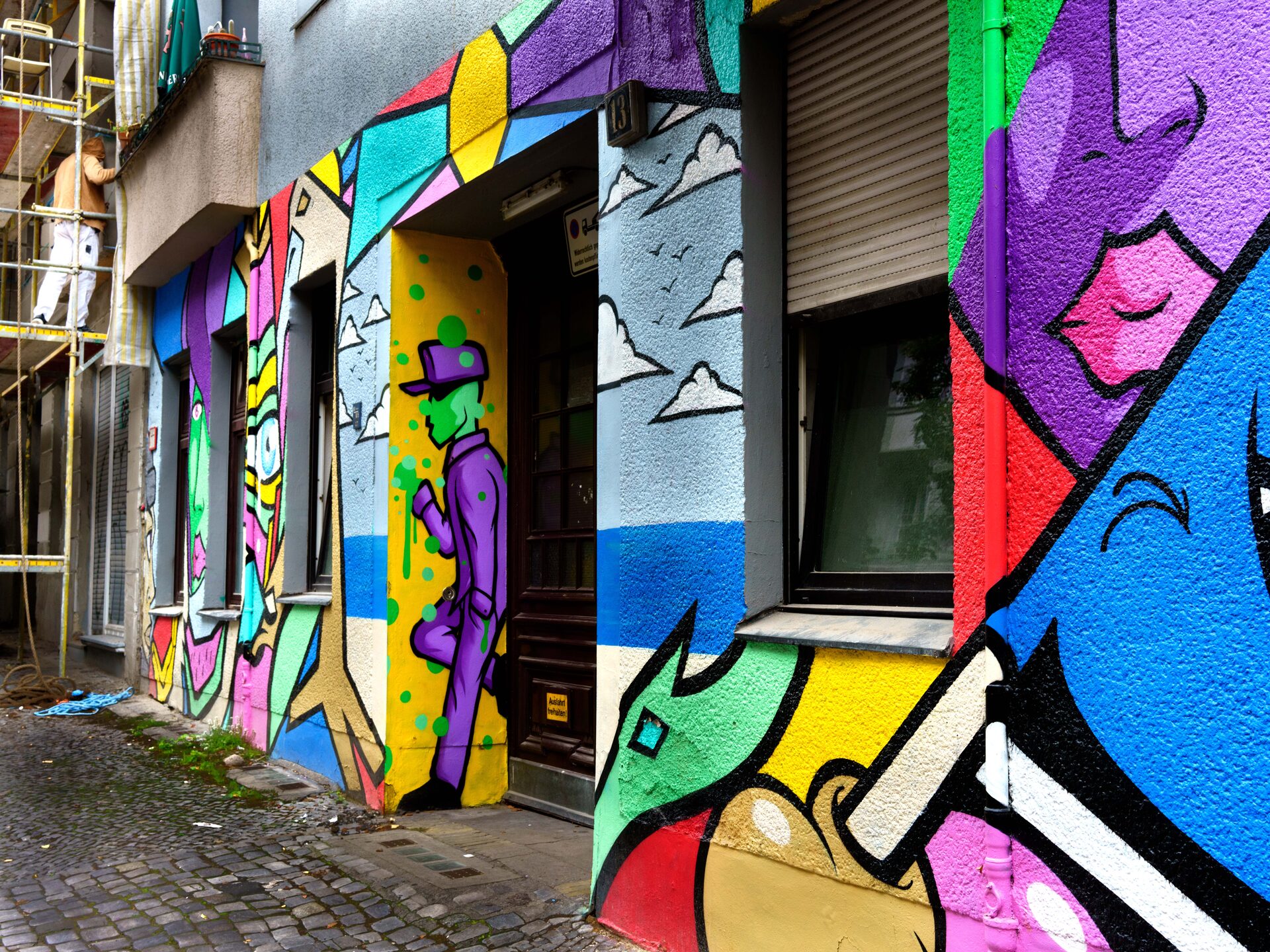 Färgsprakande gatukonst med lila figur och geometriska former på husfasad