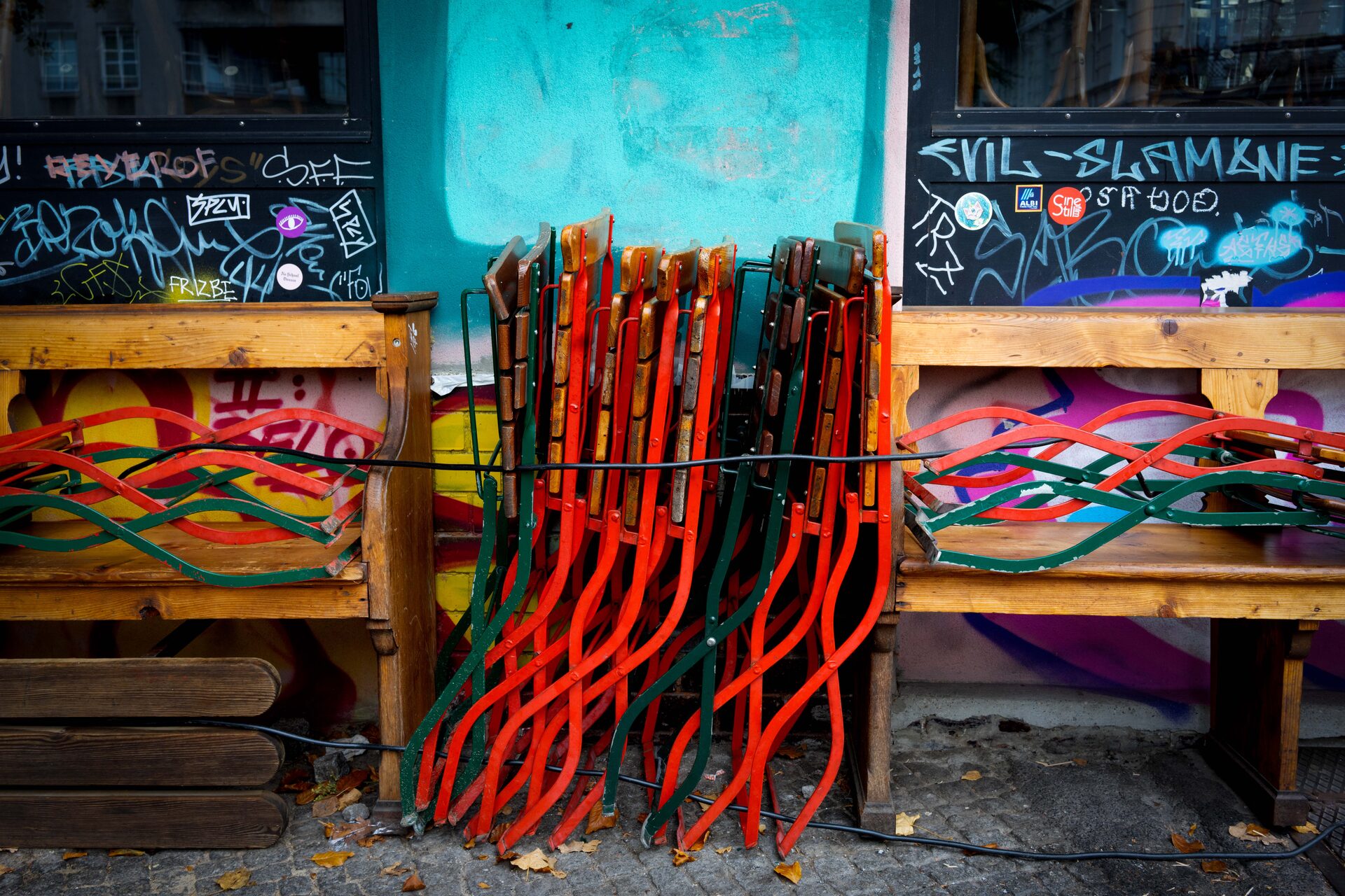 Hopfällda röda och gröna caféstolar mot graffitiklädd vägg