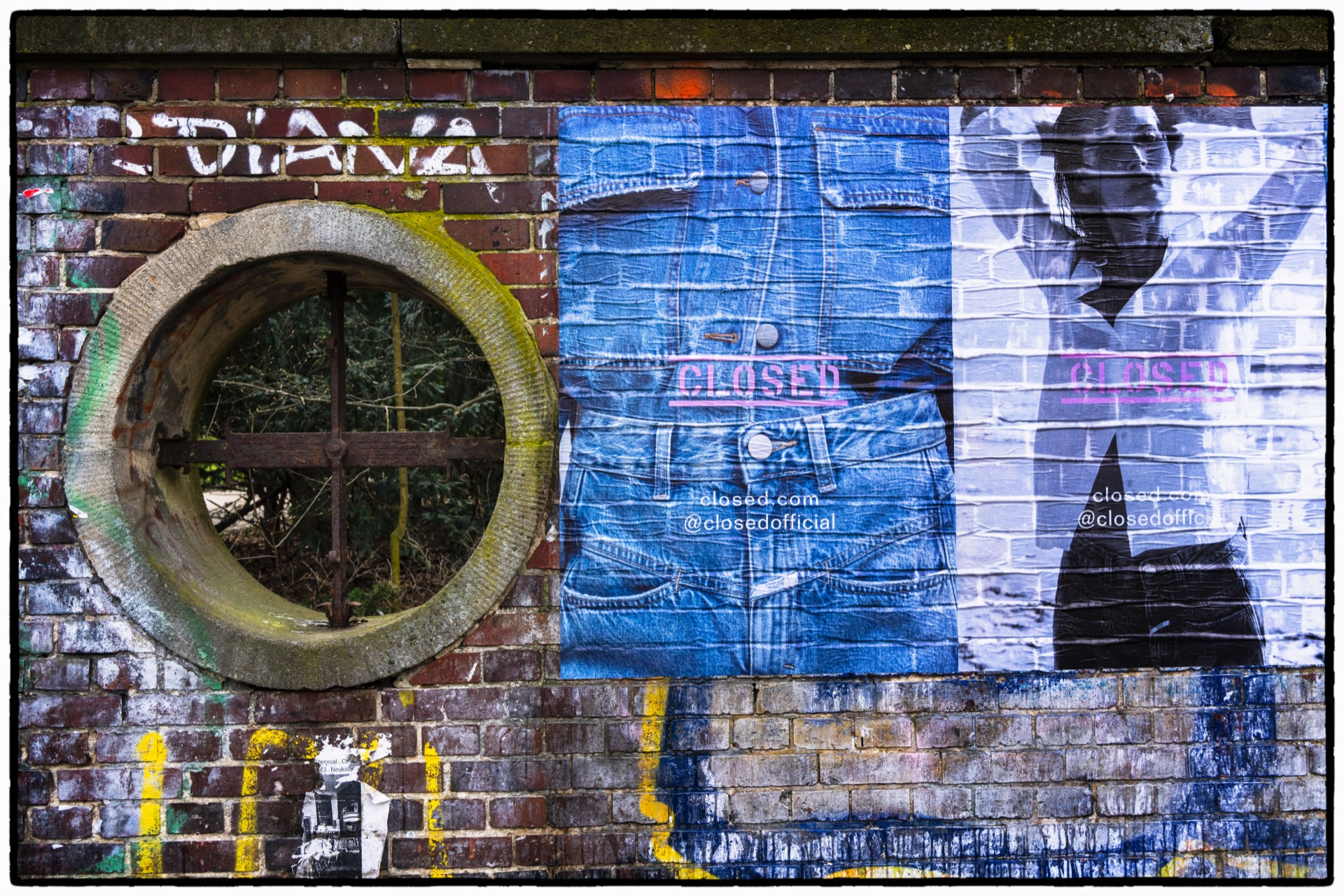 Rund fönster i tegelvägg bredvid uppklistrade jeansaffischer