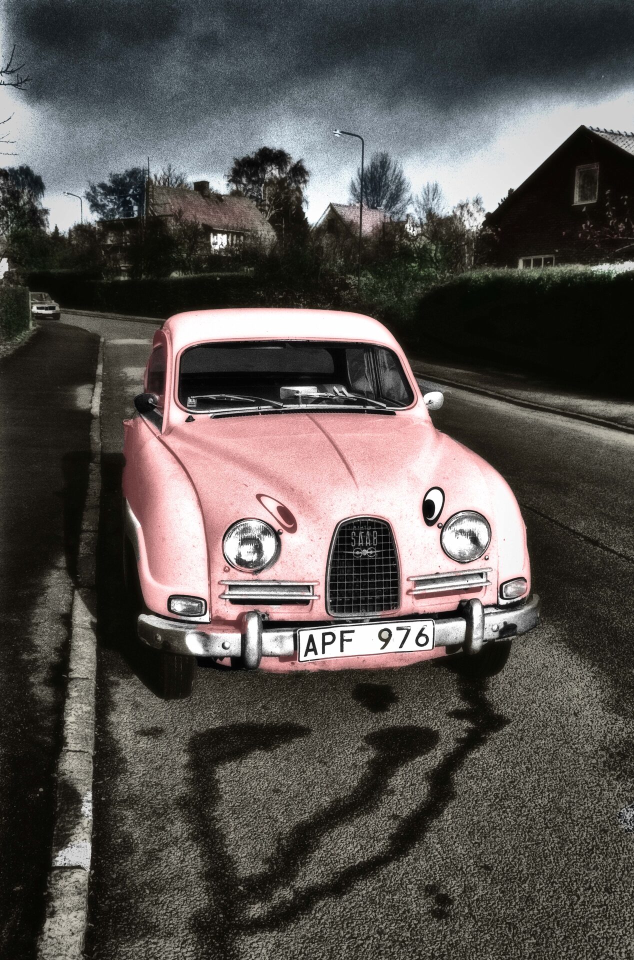 Rosa Saab 96 framifrån på villagata med dramatisk himmel