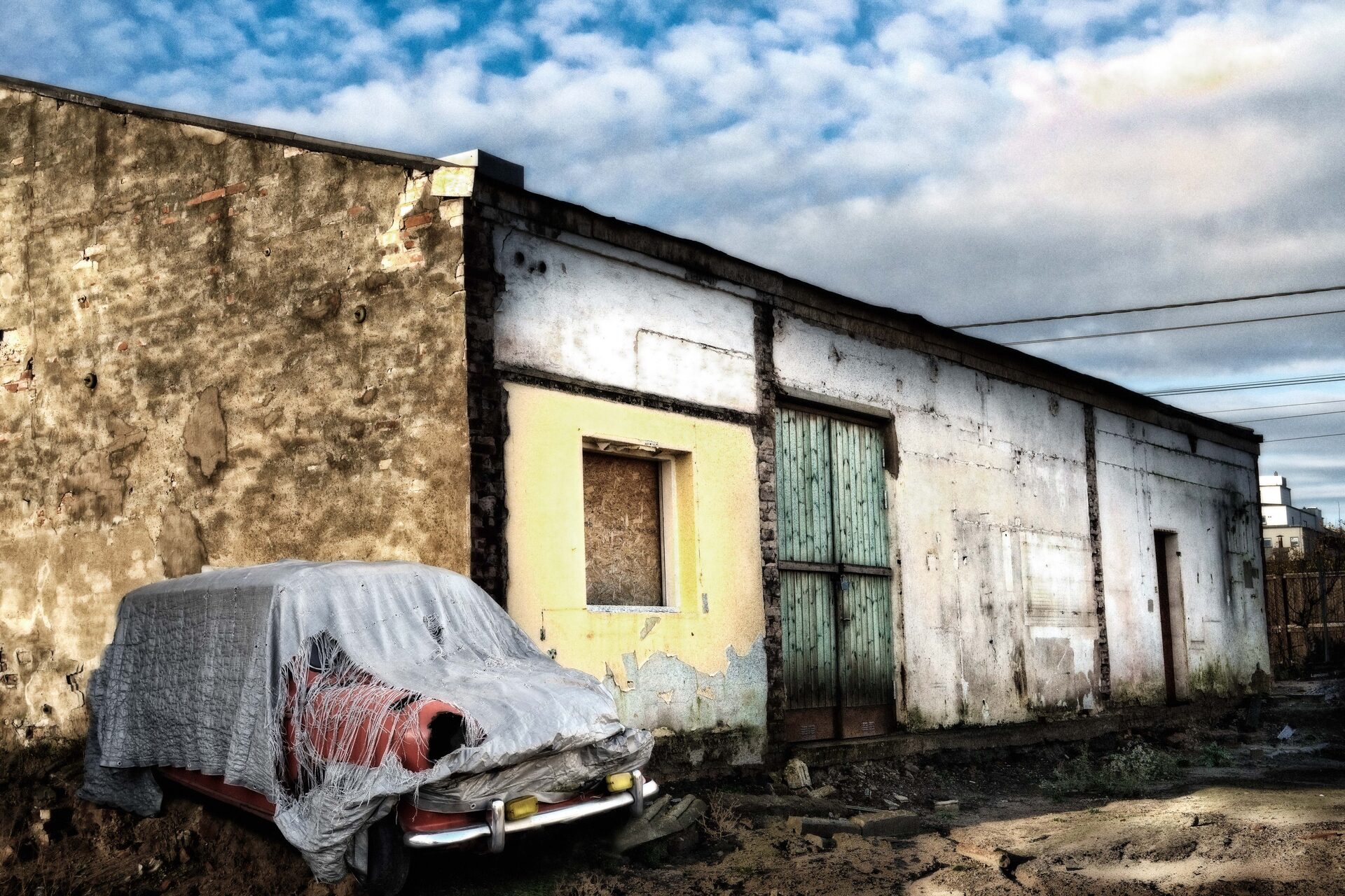 Övertäckt bil vid förfallen lagerbyggnad med dramatisk himmel