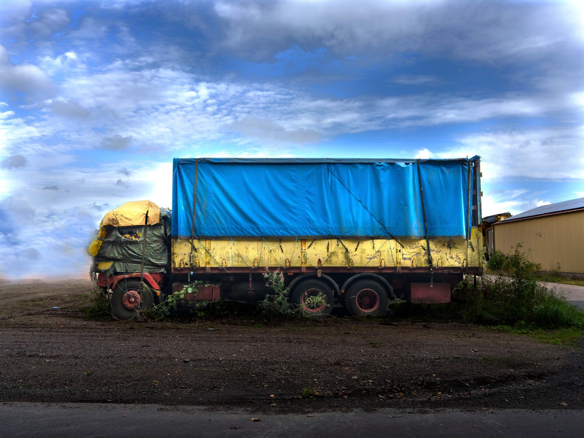 Övergiven lastbil med blå presenning mot molnig himmel