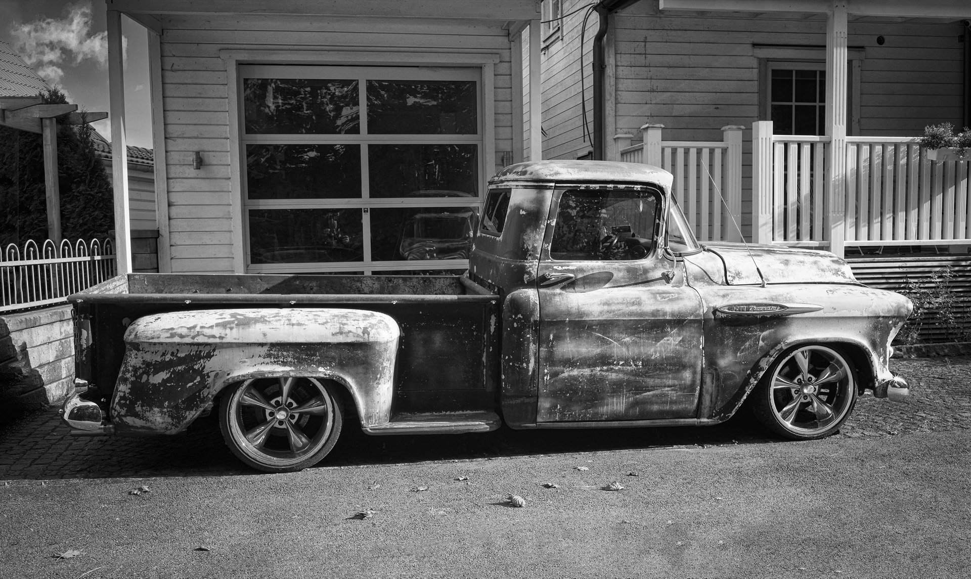 Patinerad pickup i svartvitt framför vitt trähus