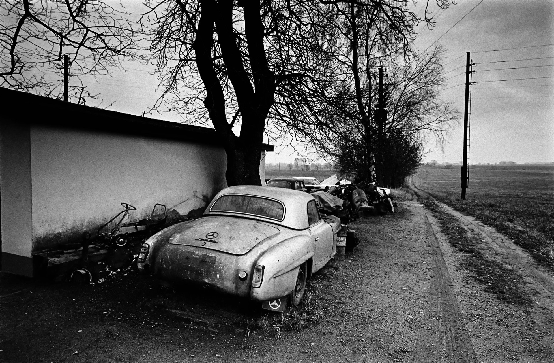 Övergiven sportbil vid landsväg med kalt träd och öppet fält