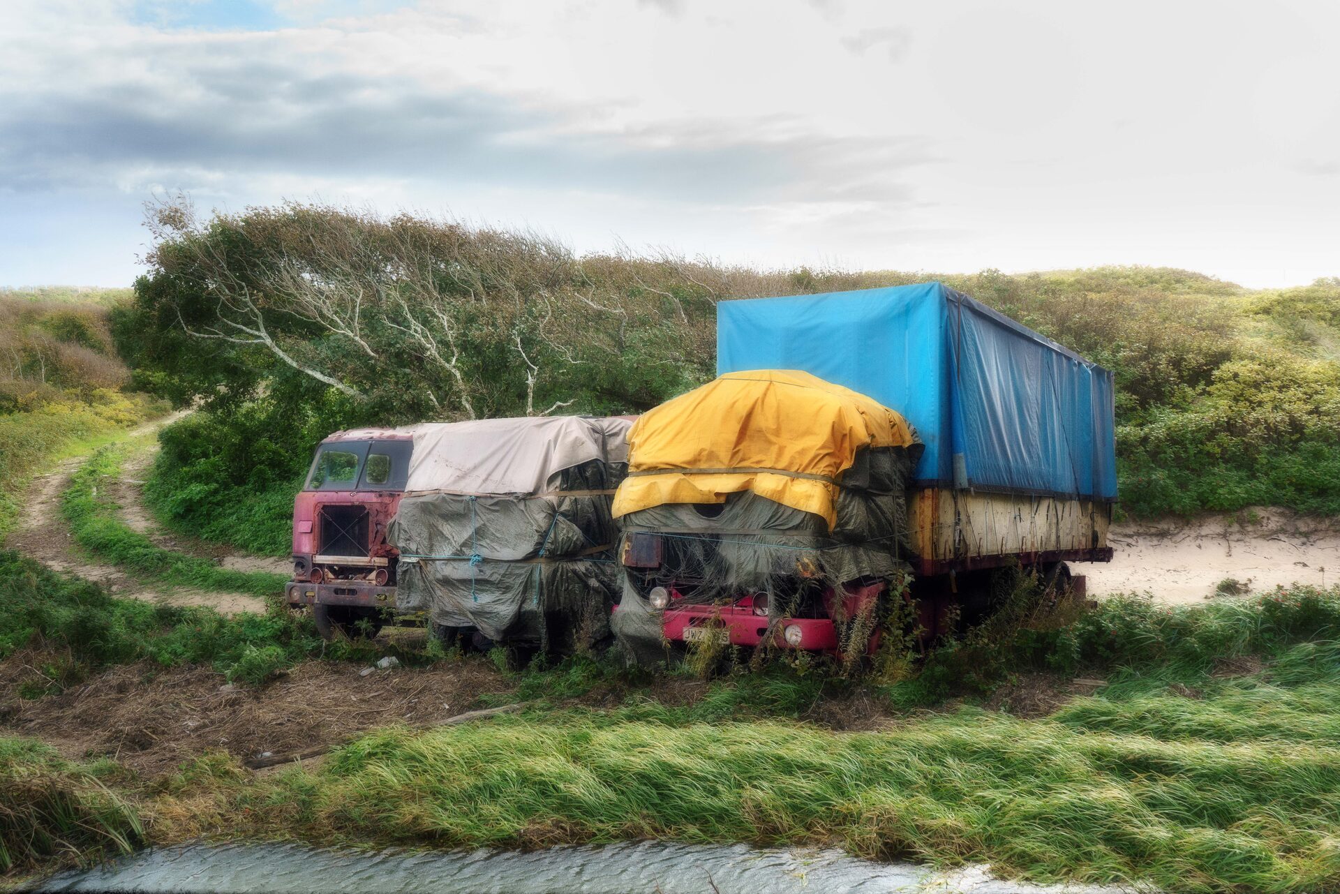 Övergivna lastbilar med färgade presenningar i sanddyner