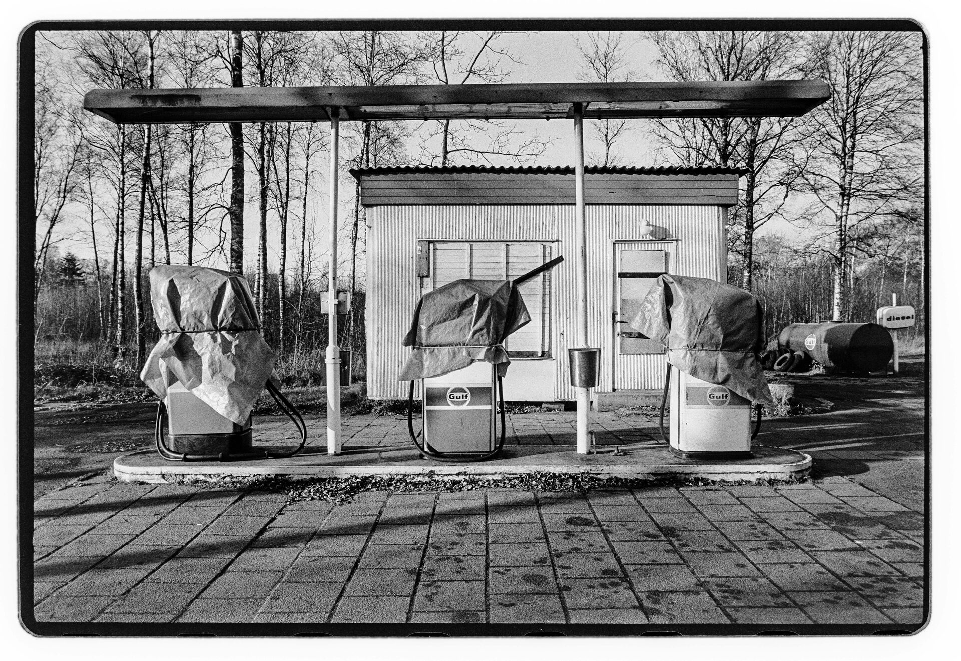 Övergiven bensinstation med insvepta pumpar, svartvitt