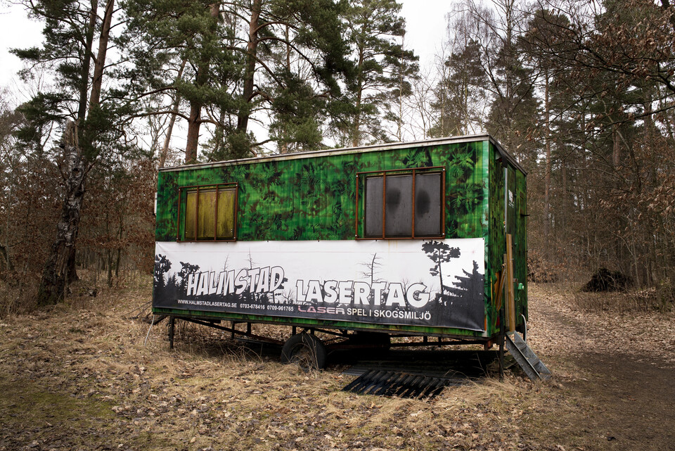 Kamouflagemålad byggvagn i tallskog med banderoll för Halmstad Lasertag
