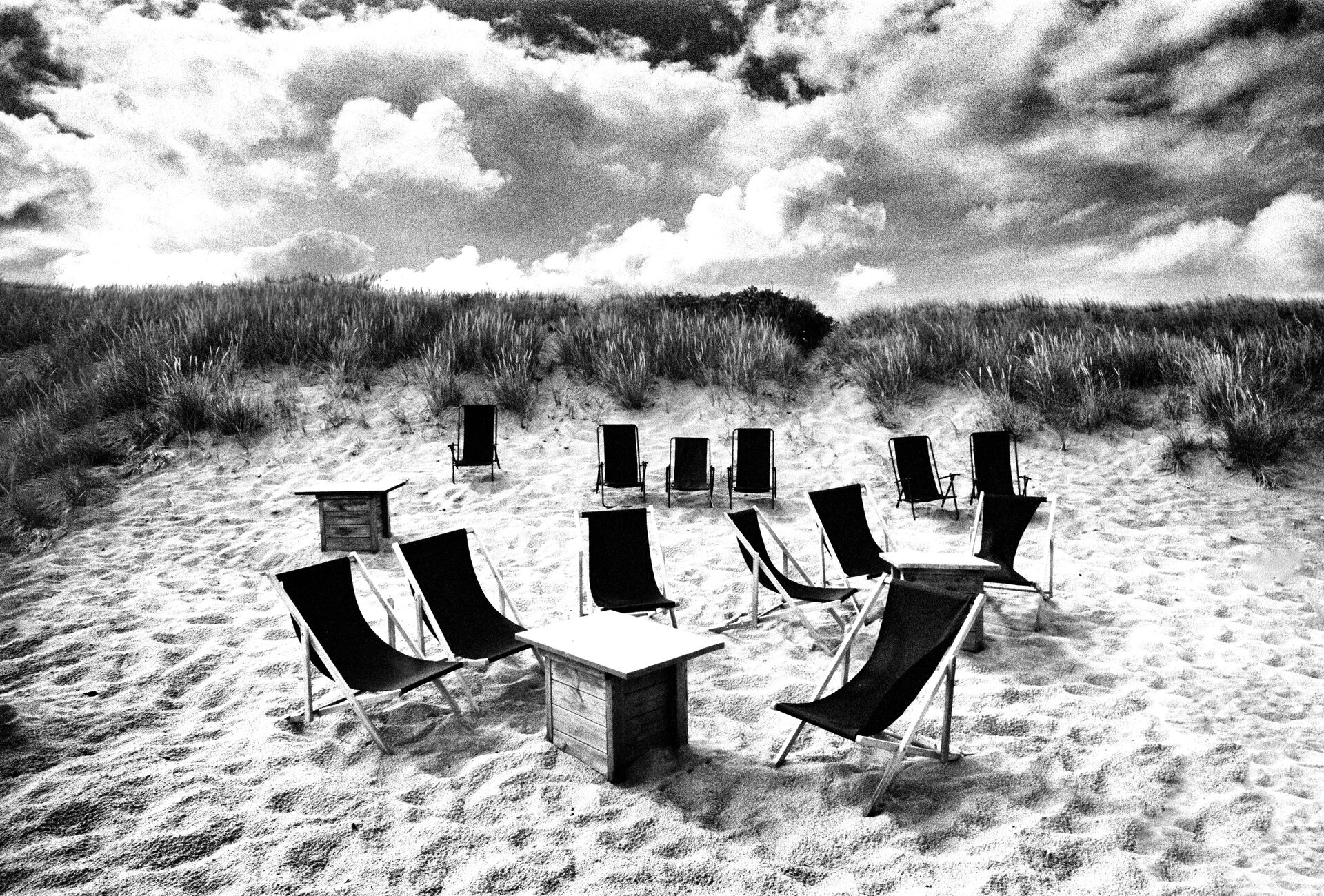 Solstolar i ring på sandstrand framför dyner, svartvitt
