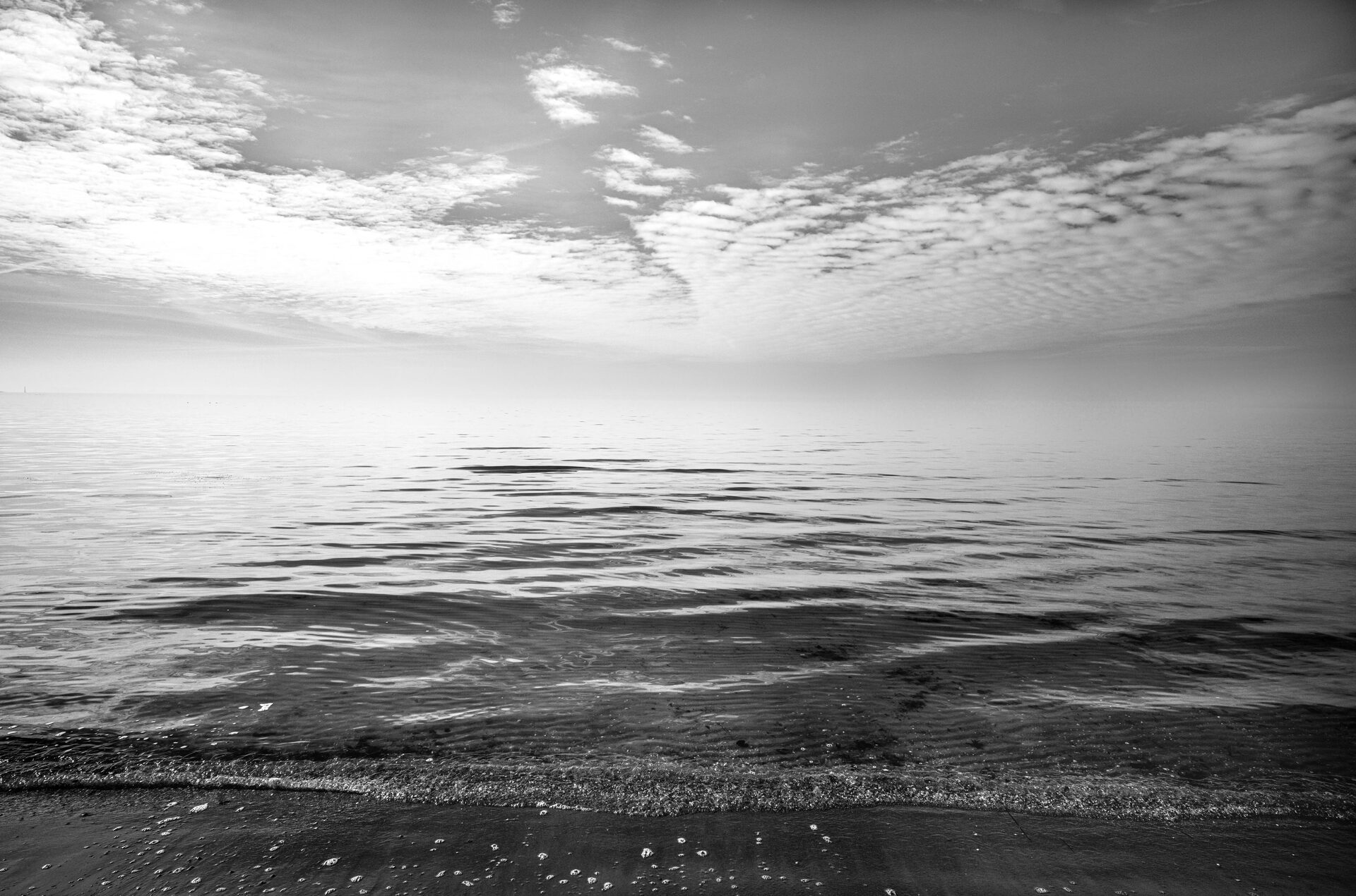 Stilla havsyta med mjuka vågor mot kvällshimmel, svartvitt