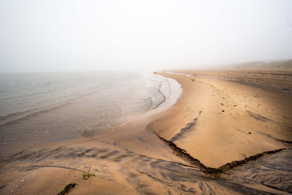 Dimh&ouml;ljd strand d&auml;r sandens &aring;dror l&ouml;per ut i stilla vatten