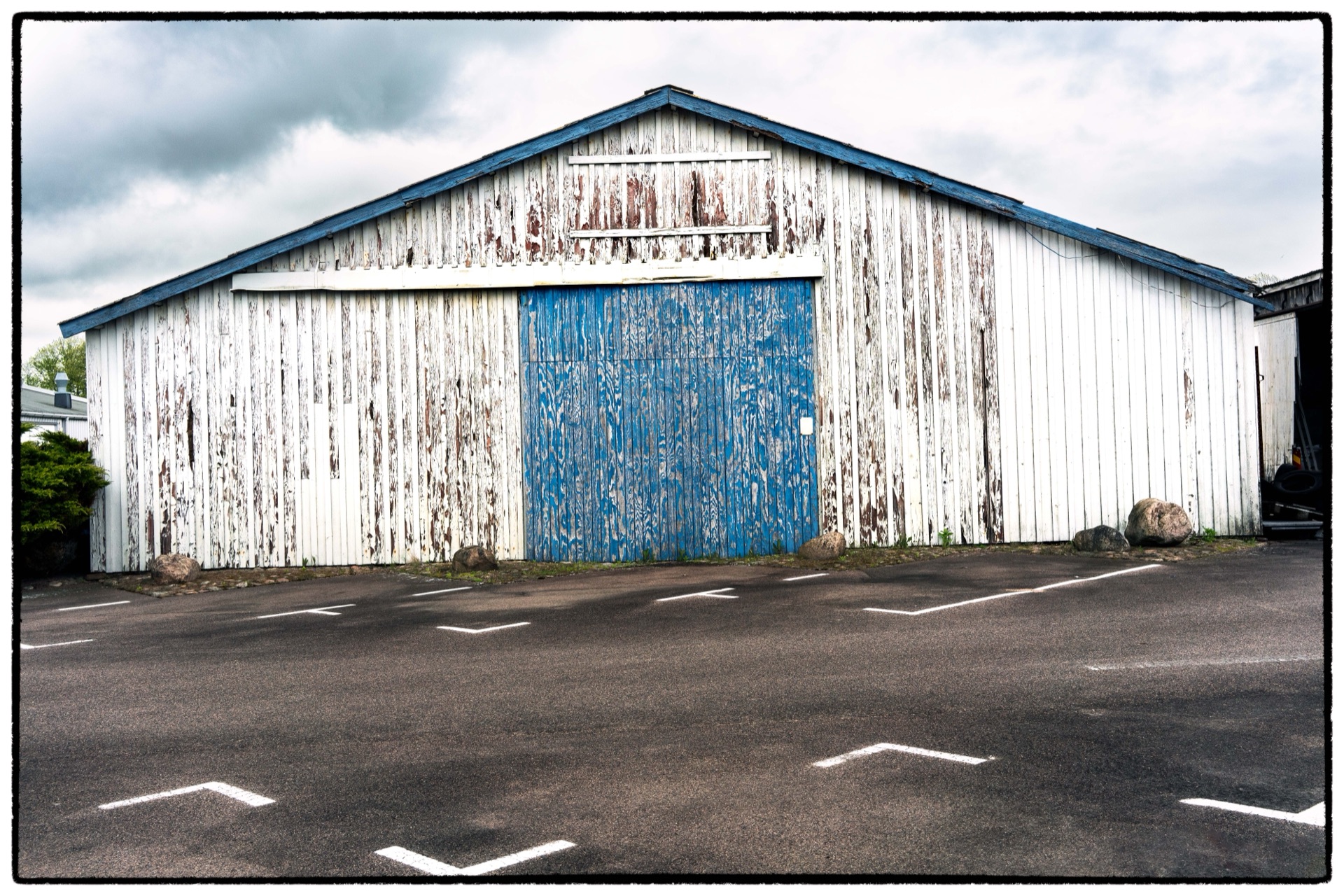 Vittrad vit lagerbyggnad med blå port och flagnad färg