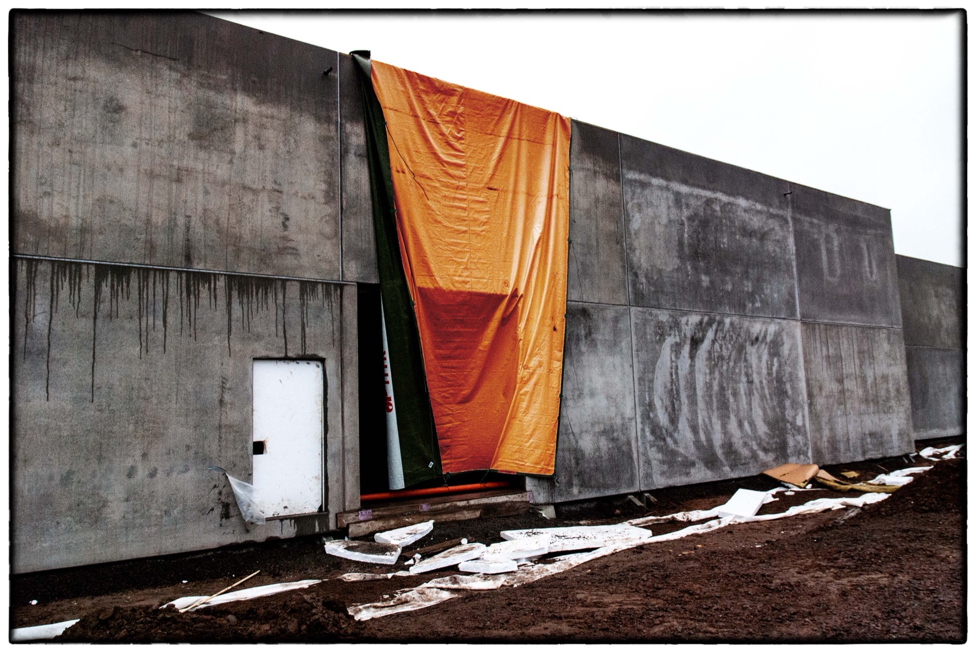 Betongbyggnad under konstruktion med orange presenning över dörr