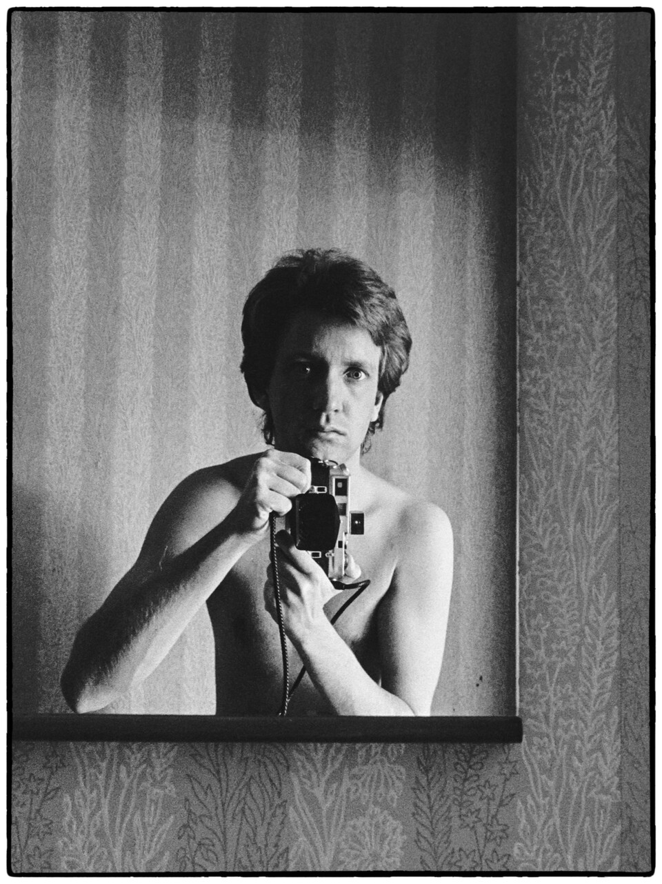 Ung man fotograferar sig själv i spegel med filmkamera, svartvitt