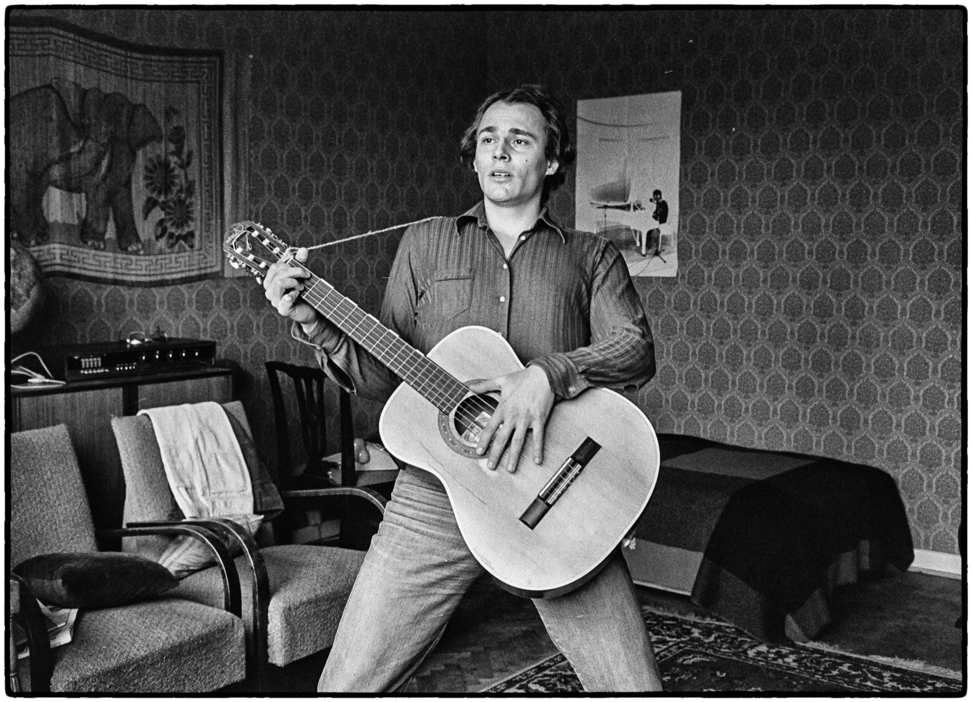 Ung man spelar akustisk gitarr i sitt rum, svartvitt