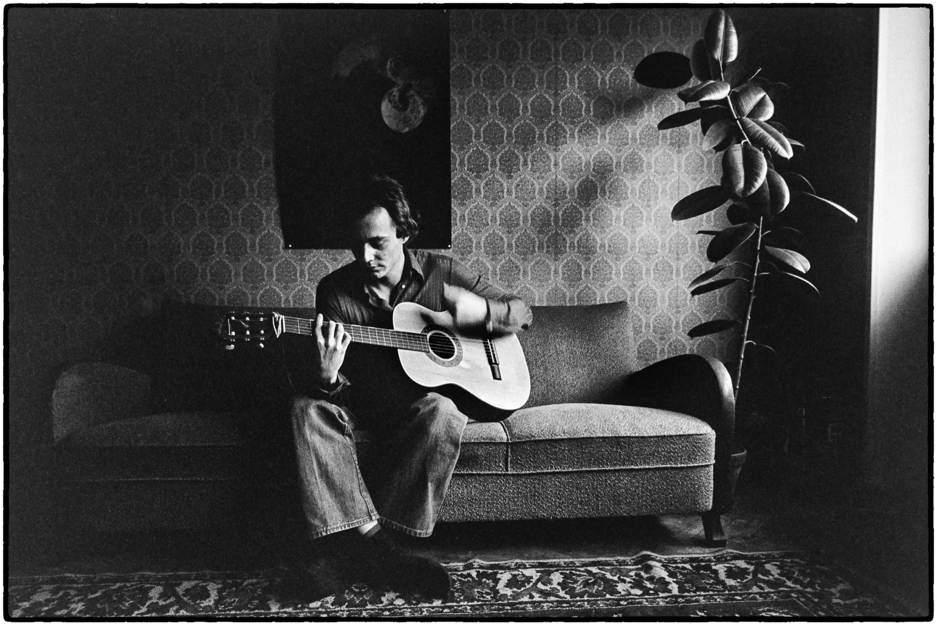 Ung man sitter och spelar gitarr i fåtölj, svartvitt