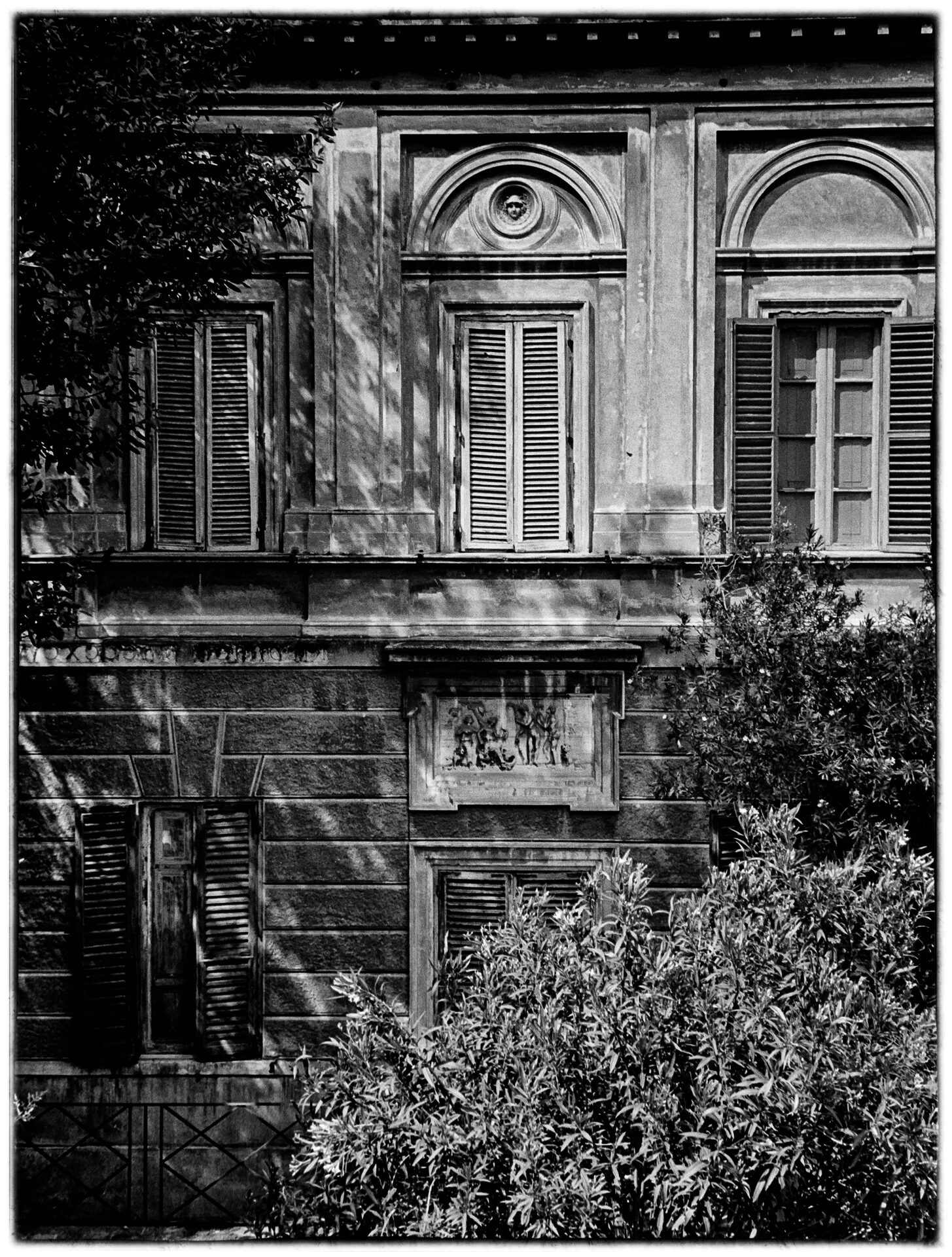 Klassisk romersk fasad med fönsterluckor och trädskuggor