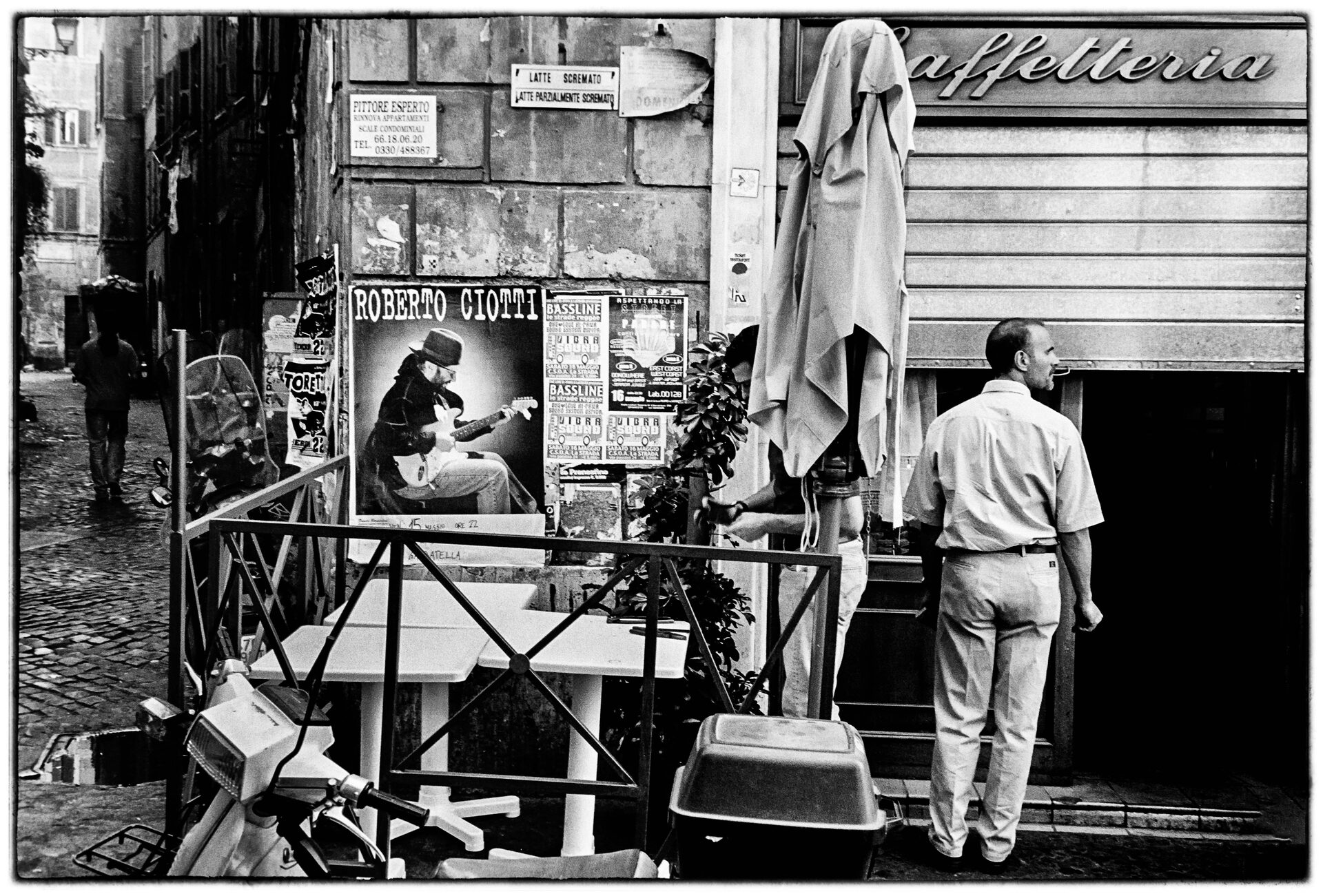 Man utanför caffetteria med konsertaffisch och hopfällda parasoll