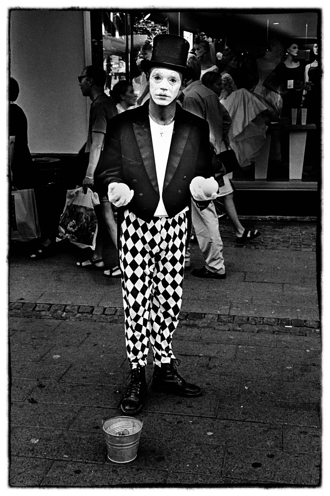 Ung gatuperformer i cylinderhatt och harlekinkläder med mugg