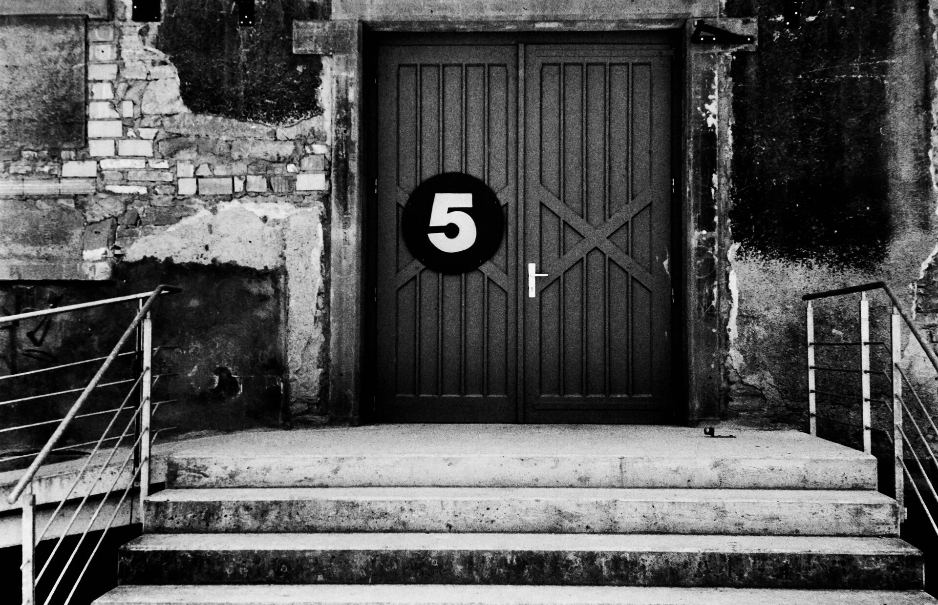 Mörk dubbeldörr med stor femma på vittrad fasad och trappräcken