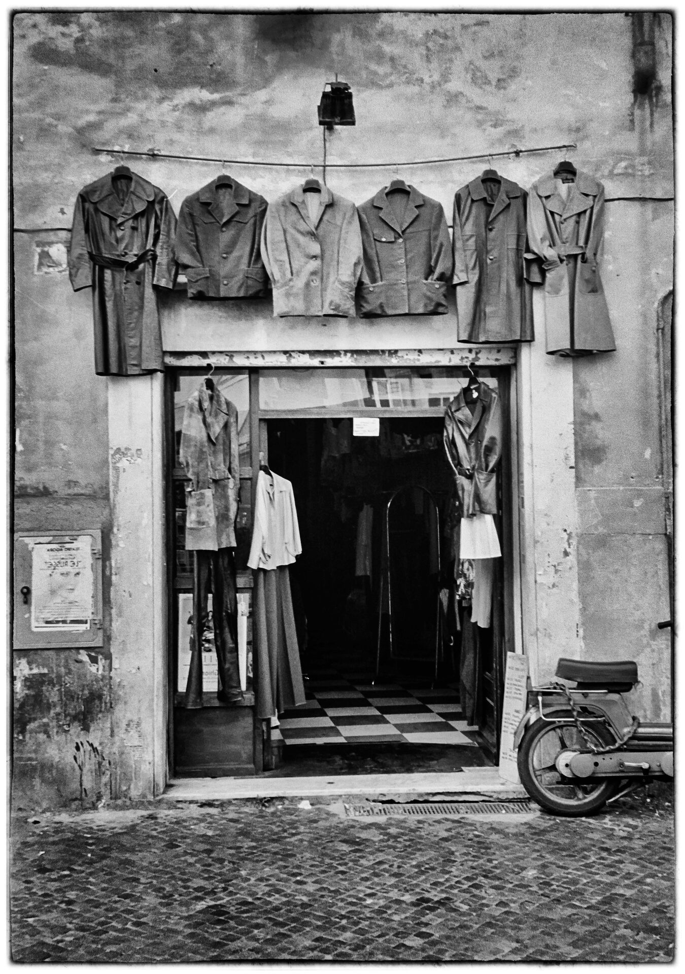 Läderjackor hänger ovanför butiksöppning på kullerstensgata med motorcykel