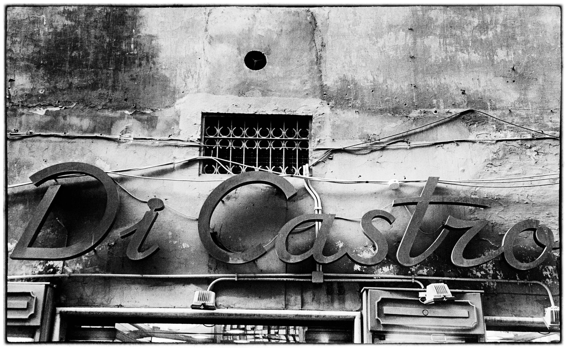 Di Castro-neonskylt på vittrad fasad med gallerfönster