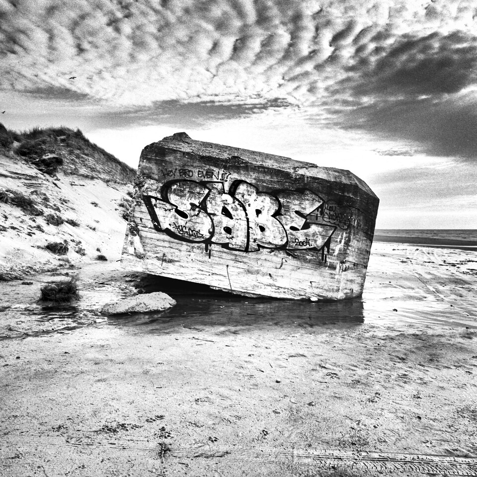 Snedställd graffitiklädd betongbunker halvt begravd i strandsanden, svartvitt