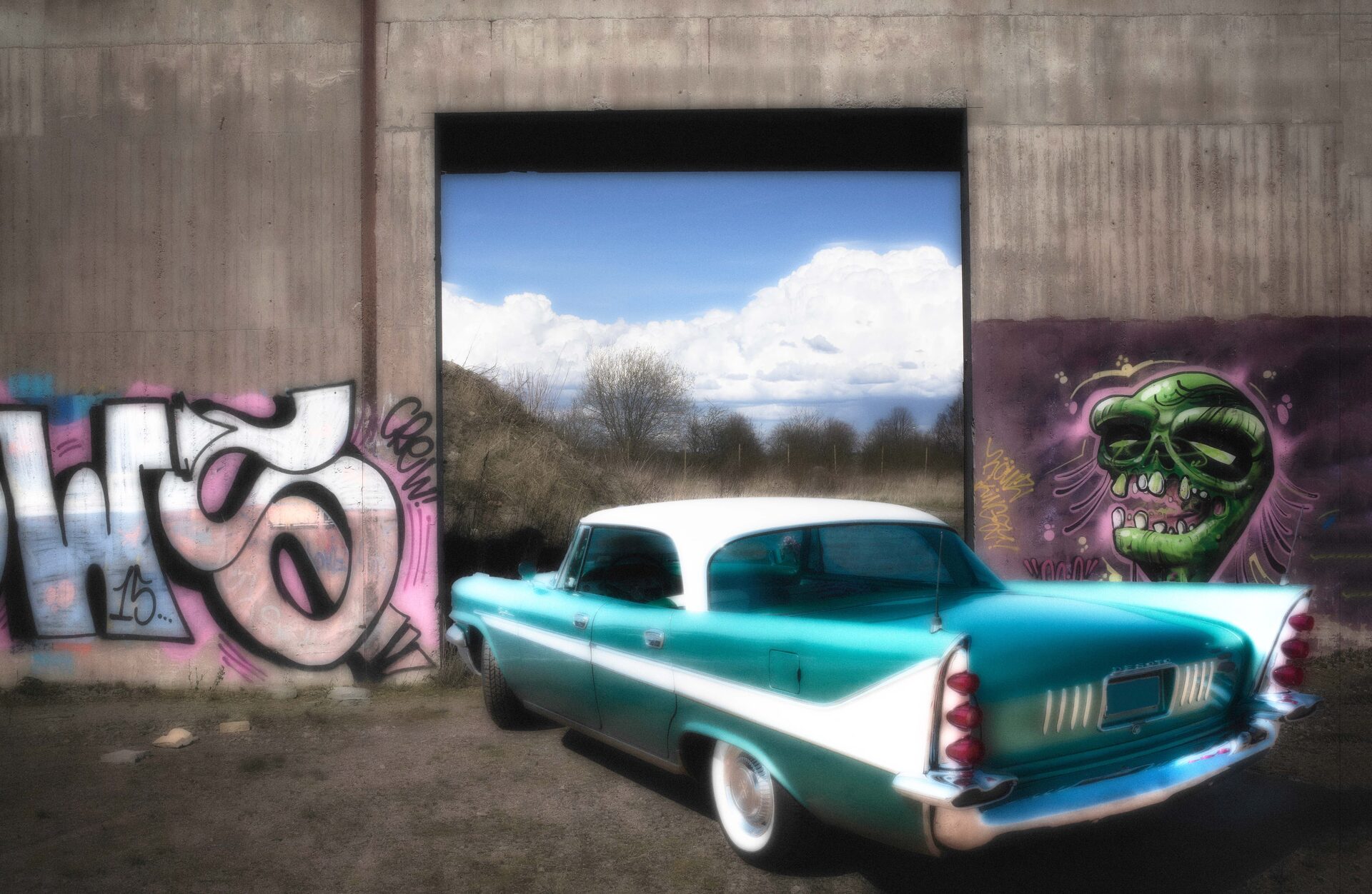 Turkos veteranbil framför graffitivägg med utsikt mot moln